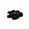 A pair of black patent leather mule sandals with buckle straps and chunky black soles, photographed on a white studio background.