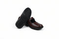 A pair of dark brown leather Mary Jane shoes with black soles, with one shoe standing upright to show the sole and the other lying on its side showing the side profile.