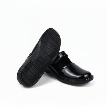 A pair of black leather slip-on shoes, with one shoe standing upright to show the textured black sole and the other lying on its side to display the glossy black toe cap, set against a plain white studio background.