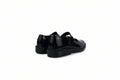 A pair of black patent leather Mary Jane shoes with strap closures, shown from a side-rear angle against a white studio backdrop.