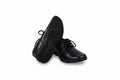 A pair of black lace-up dress shoes, with one shoe standing upright to show the textured black sole and the other lying on its side to show the black leather upper, set against a plain white studio background.