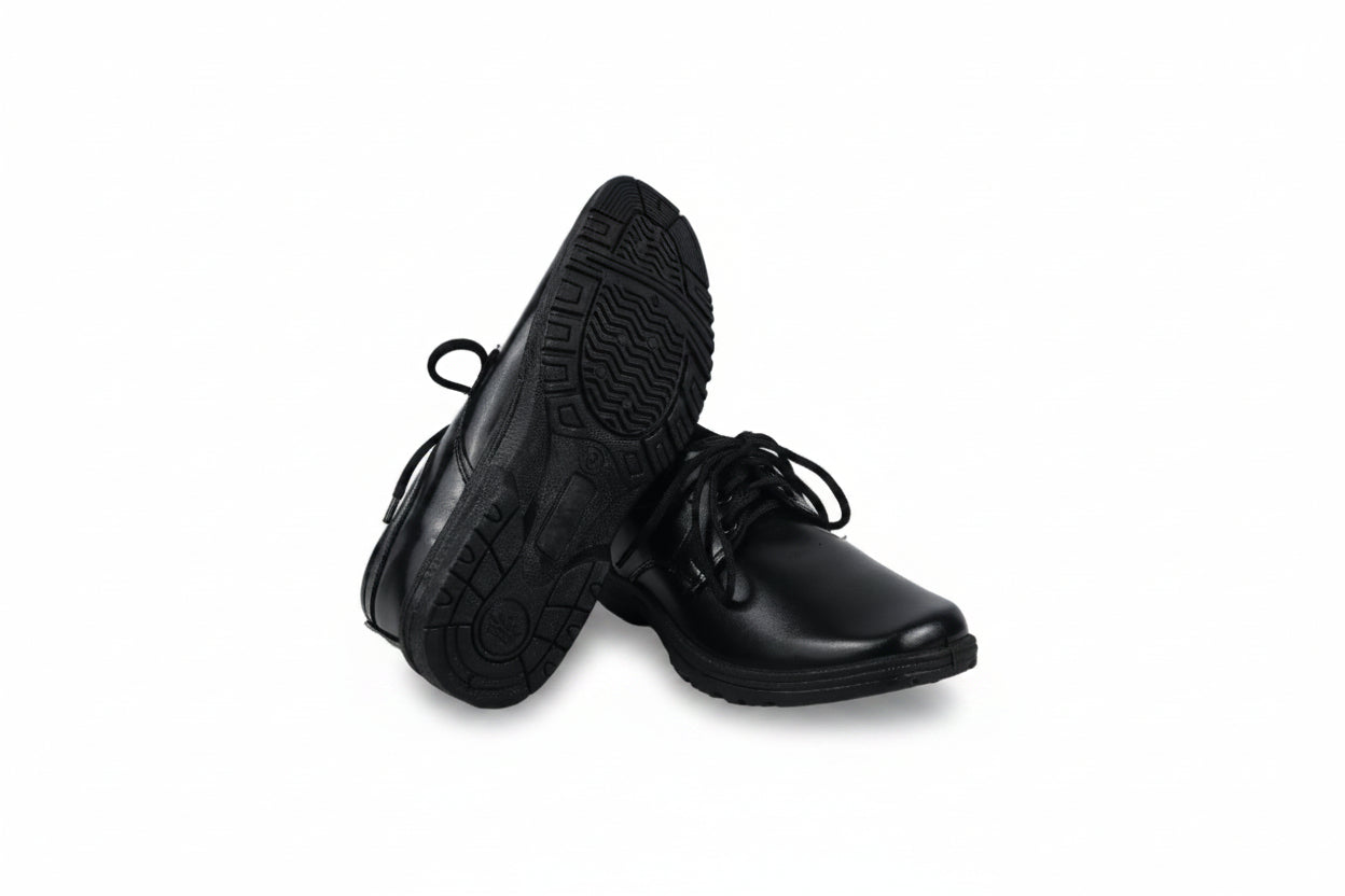 A pair of black lace-up dress shoes, with one shoe standing upright to show the textured black sole and the other lying on its side to show the black leather upper, set against a plain white studio background.