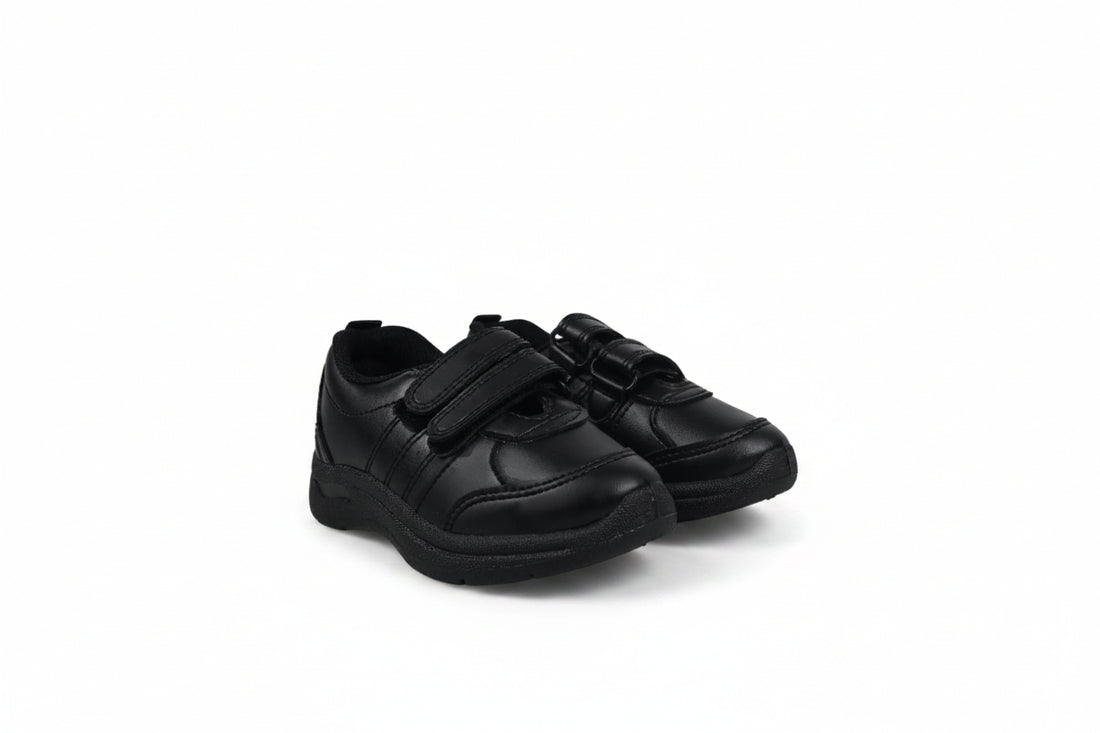 A pair of black children's low-top sneakers with hook-and-loop strap closures, photographed on a light gray studio background.