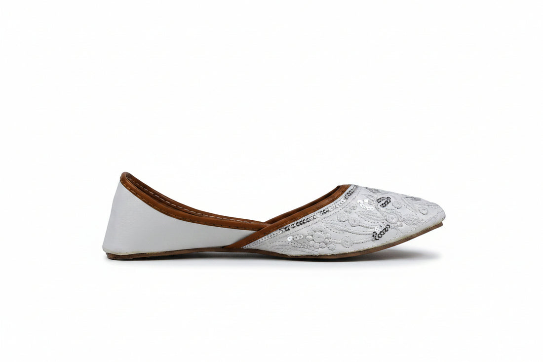 A pair of white embroidered flat shoes with brown insoles, photographed on a light gray studio background.