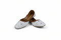 A pair of white embroidered flat shoes with brown insoles, photographed on a light gray studio background.