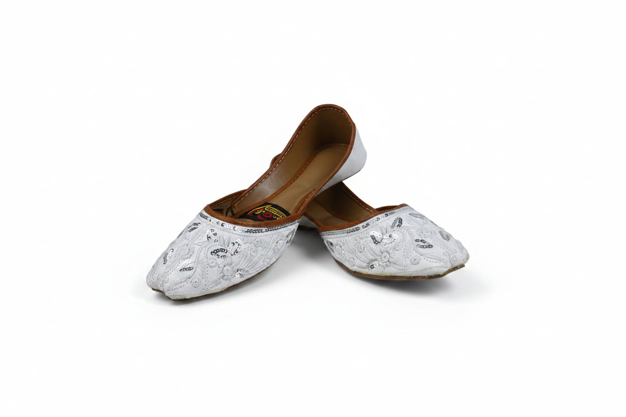 A pair of white embroidered flat shoes with brown insoles, photographed on a light gray studio background.