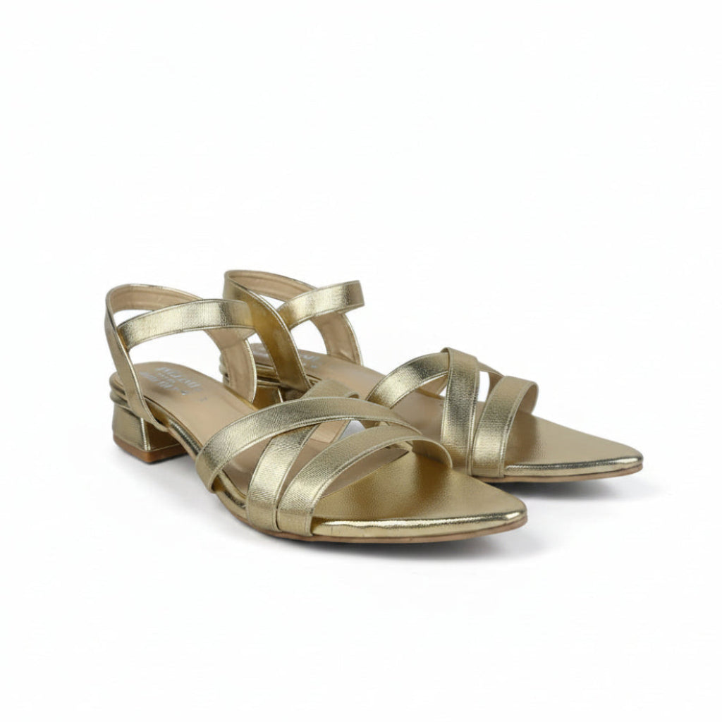 A pair of metallic gold strappy sandals with low block heels and pointed toes, shown on a light gray background.