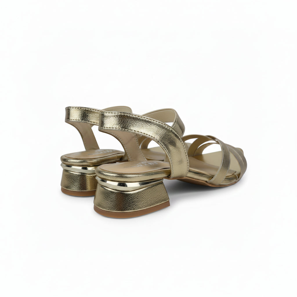A pair of metallic gold strappy slingback sandals with low block heels, shown on a light gray fabric studio background.
