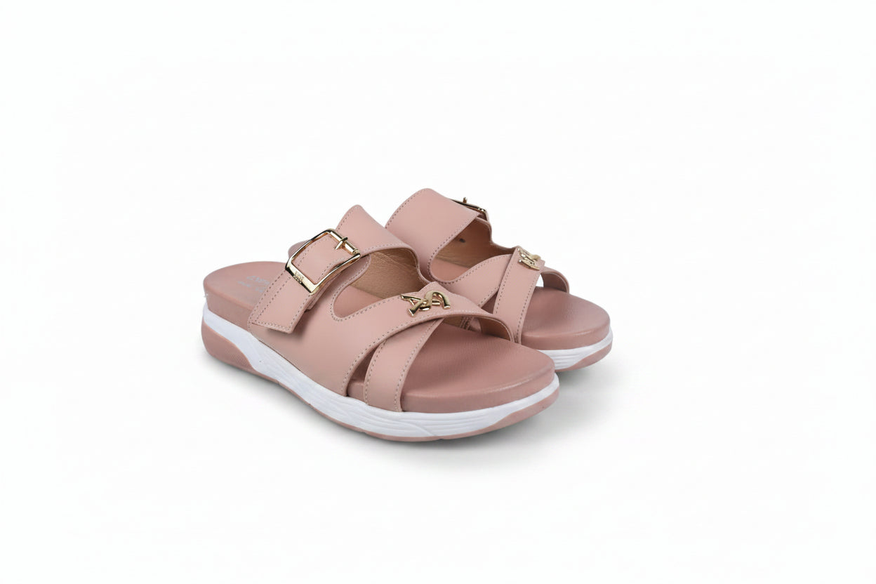 A pair of women's open-toe slide sandals in a dusty pink color, featuring double adjustable straps with gold-tone buckles and a small gold monogram logo on the front strap, set against a plain white background.