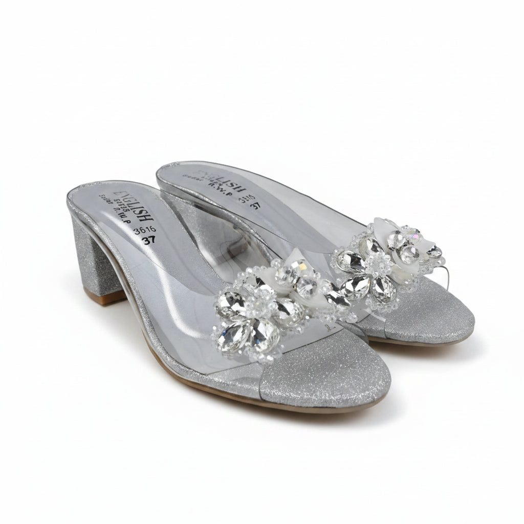 A pair of silver glitter mule sandals with clear rhinestone floral embellishments on the straps, shown against a plain white background.