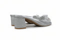 A single silver glitter mule sandal with a chunky block heel and floral embellishments on the toe strap, shown against a plain white background.