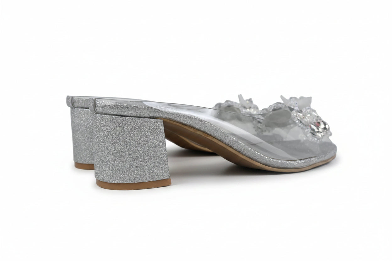 A single silver glitter mule sandal with a chunky block heel and floral embellishments on the toe strap, shown against a plain white background.