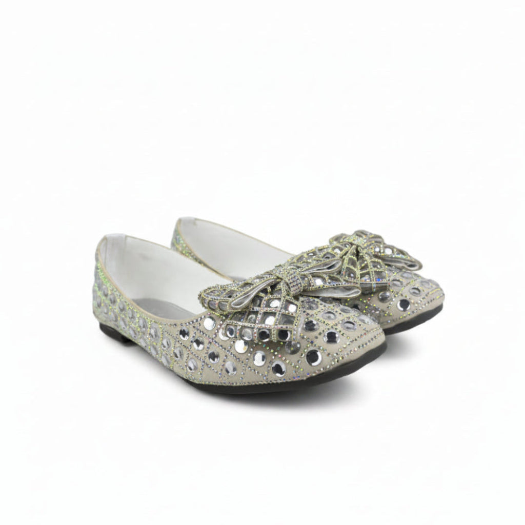 A pair of silver glitter flat shoes embellished with rhinestones and a large decorative bow on the toe, shown against a plain white background.