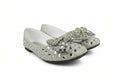 A pair of silver glitter flat shoes embellished with rhinestones and a large decorative bow on the toe, shown against a plain white background.