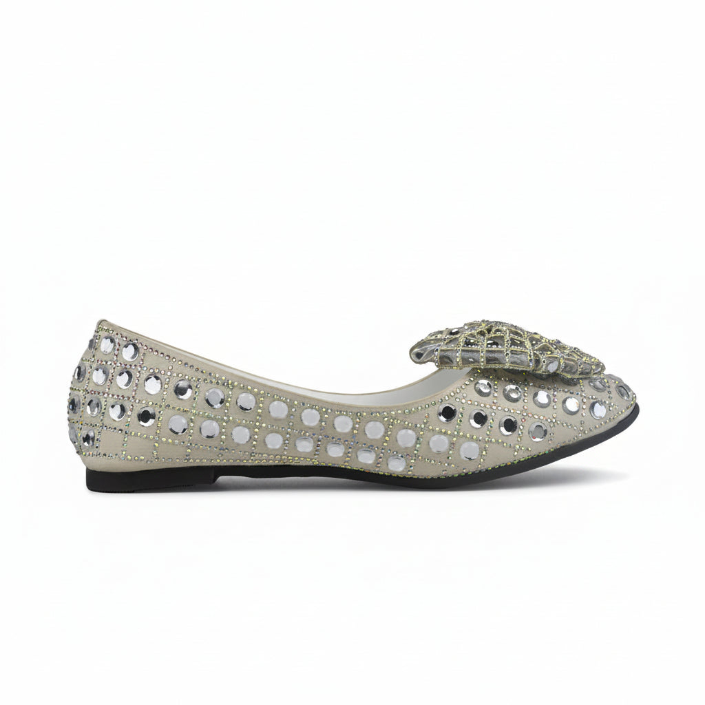 A pair of silver glitter flat shoes embellished with rhinestones and a large decorative bow on the toe, shown against a plain white background.