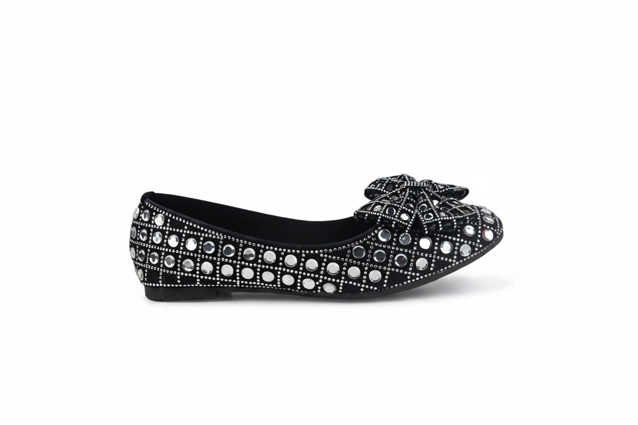 A single black flat shoe decorated with rows of silver rhinestones and a matching rhinestone-embellished bow on the toe, shown against a plain white background.