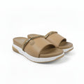 A pair of women's slide sandals in tan with a gold-tone chain detail across the top and a white sole, shown against a light gray background.
