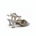 A pair of women's heeled sandals with silver glittery toe caps, ankle straps, and flared block heels, shown on a light gray background.