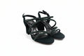 A pair of black strappy high-heeled sandals with textured, glittery greenish-gray straps, shown on a light gray studio background.