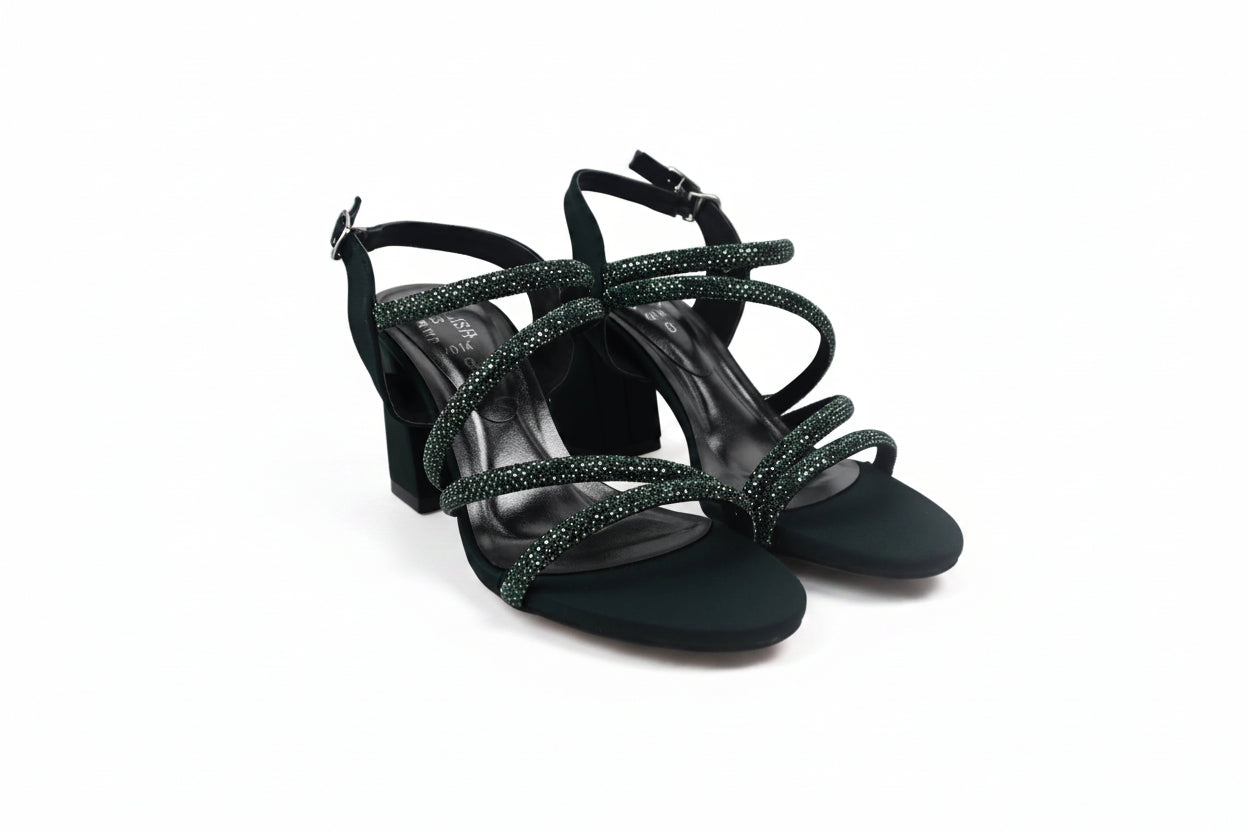 A pair of black strappy high-heeled sandals with textured, glittery greenish-gray straps, shown on a light gray studio background.