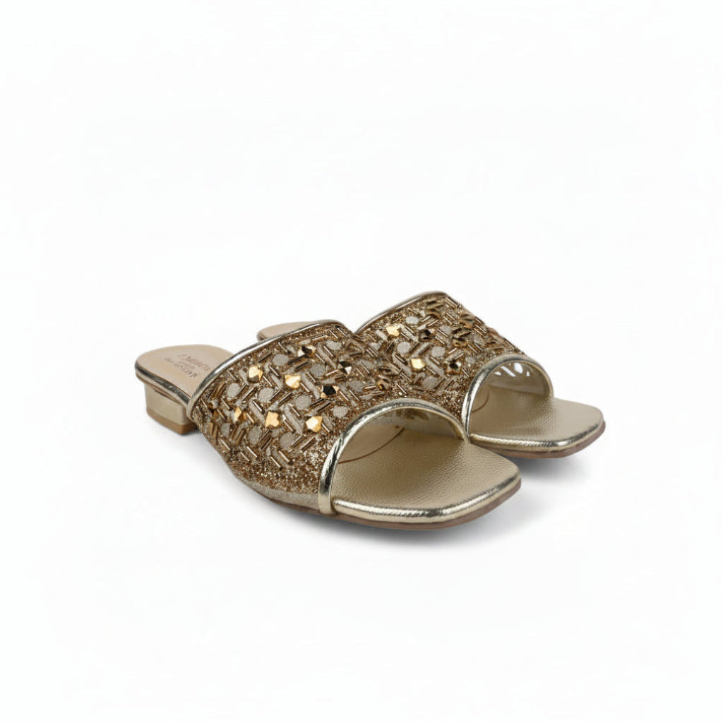 A pair of metallic gold slide sandals with intricate woven and rhinestone embellishments on the straps, set against a plain white background.