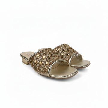 A pair of metallic gold slide sandals with intricate woven and rhinestone embellishments on the straps, set against a plain white background.