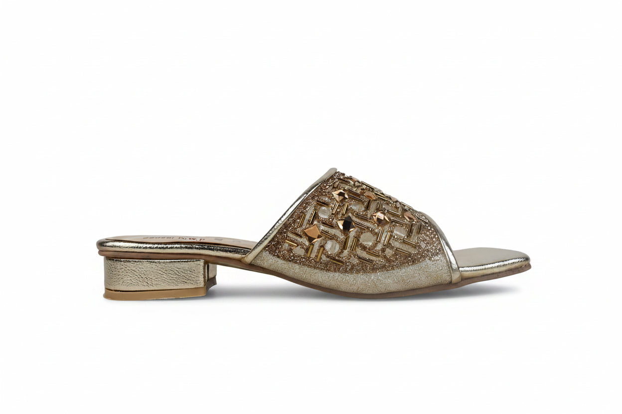A single women's heeled mule sandal in metallic gold, featuring an intricate geometric patterned upper and a low block heel, shown against a neutral light gray background.