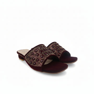 A pair of women's open-toe slide sandals in deep burgundy velvet, featuring a wide embellished strap with dark red rhinestones and gold-toned metal details, set against a plain white background.