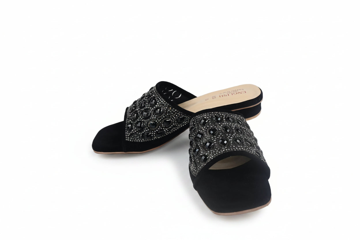 A pair of black suede mule sandals with wide straps heavily embellished with silver rhinestones, shown on a white studio background.
