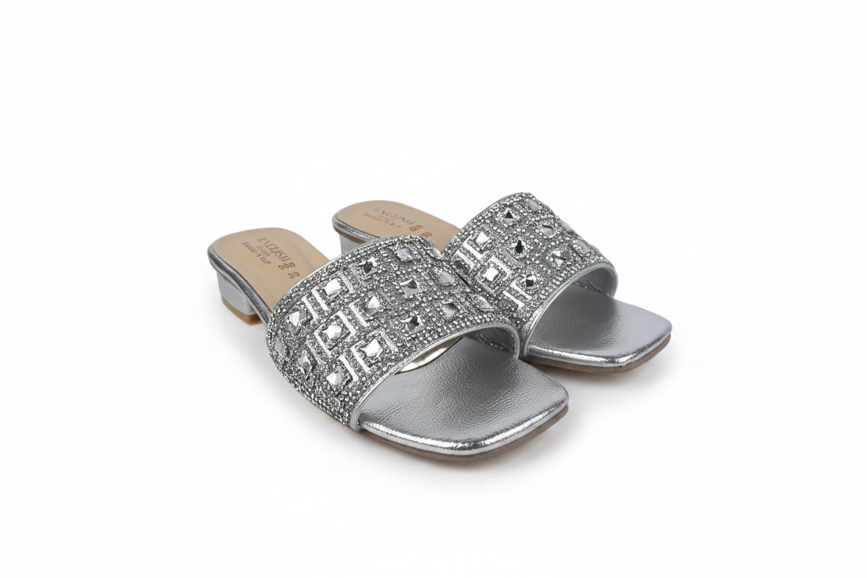 A pair of women's silver slide sandals with geometric rhinestone embellishments on the straps, set against a plain white background.