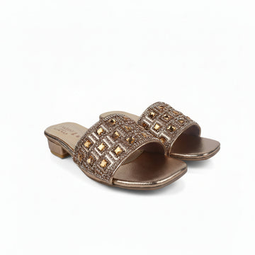 A pair of metallic rose gold slide sandals with geometric rhinestone embellishments on the straps and a low block heel, shown on a light gray background.