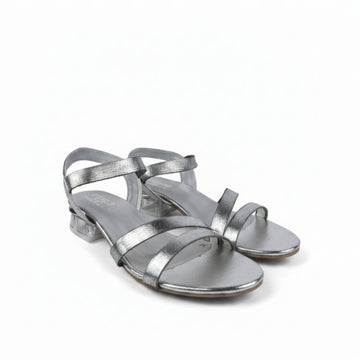 A pair of metallic silver strappy sandals with low block heels, shown on a light gray fabric background.