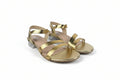 A pair of women's metallic gold strappy sandals with low block heels, shown on a light gray fabric background.
