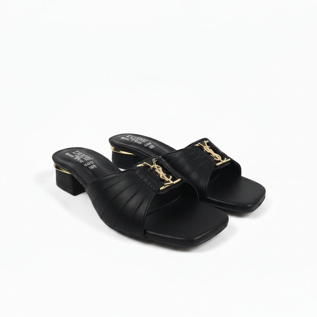 A pair of black leather slide sandals with a low block heel and a gold-tone metal YSL logo buckle, shown on a light gray background.