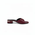 A single burgundy leather mule sandal with a low block heel and a gold-tone metal accent on the strap, shown from a side profile against a light gray background.