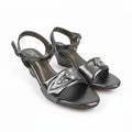 A pair of metallic silver heeled sandals with ankle straps and decorative embellishments on the toes, photographed on a white background.