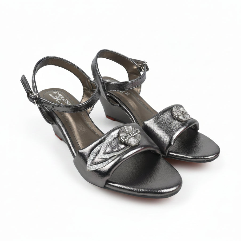 A pair of metallic silver heeled sandals with ankle straps and decorative embellishments on the toes, photographed on a white background.