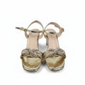 A pair of metallic gold high-heeled sandals with criss-cross embellished straps and rhinestone detailing, shown on a light gray background.
