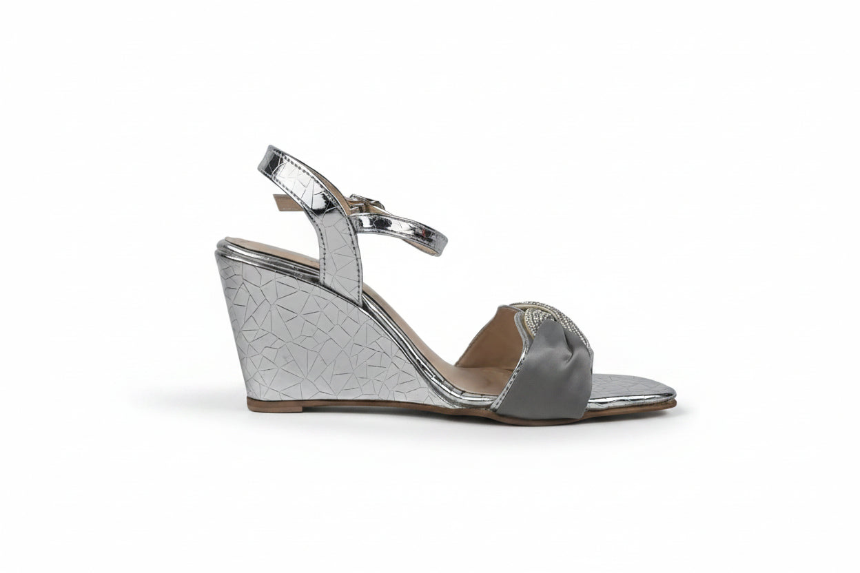 A single women's wedge sandal in metallic silver with a textured pattern on the wedge and a satin bow detail on the toe, shown against a light gray background.