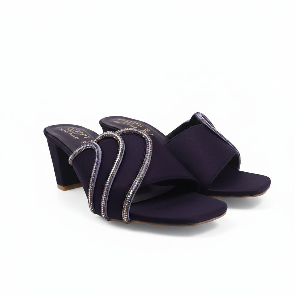 A pair of black heeled mule sandals with wide straps decorated with silver rhinestone-like trim, photographed on a plain light background.