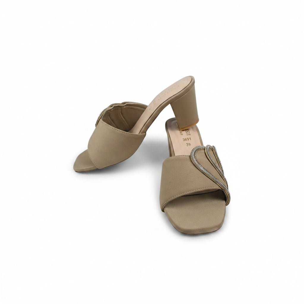 A pair of beige open-toe mule sandals with block heels, featuring one sandal with a plain strap and the other with a decorative rhinestone-embellished strap, set against a white studio background.