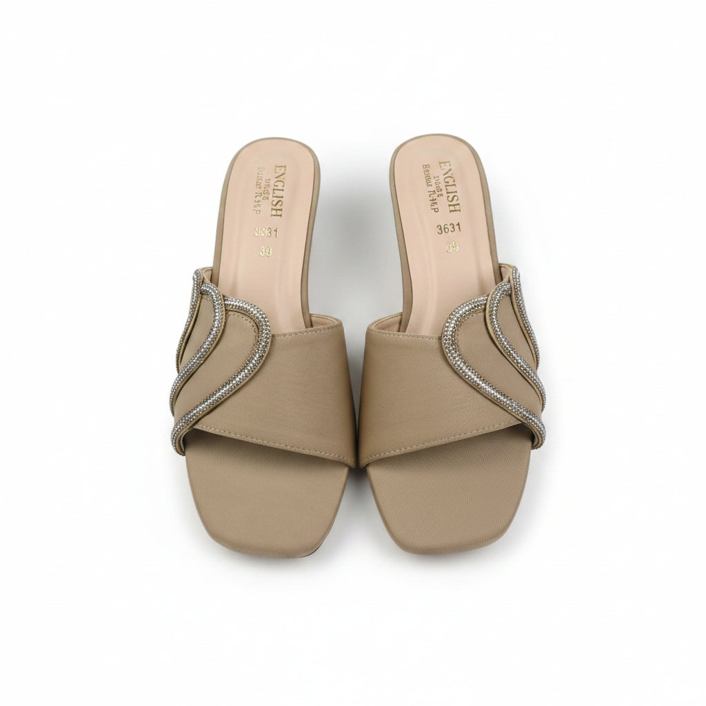 A pair of beige slide sandals with square toes and embellished straps featuring a curved design set with small clear rhinestones, shown on a light gray surface.