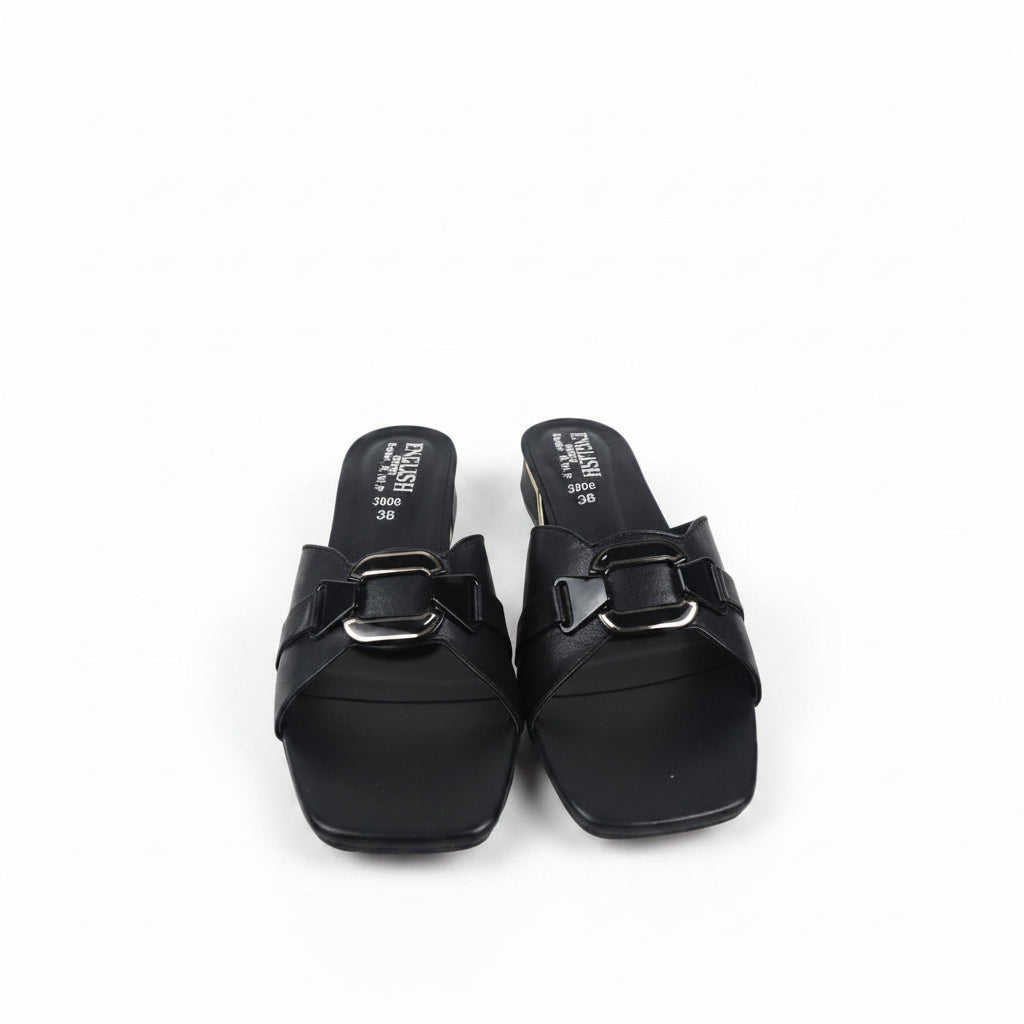 A pair of black leather slide sandals with square toes and wide straps featuring a prominent silver buckle, shown on a light gray surface.
