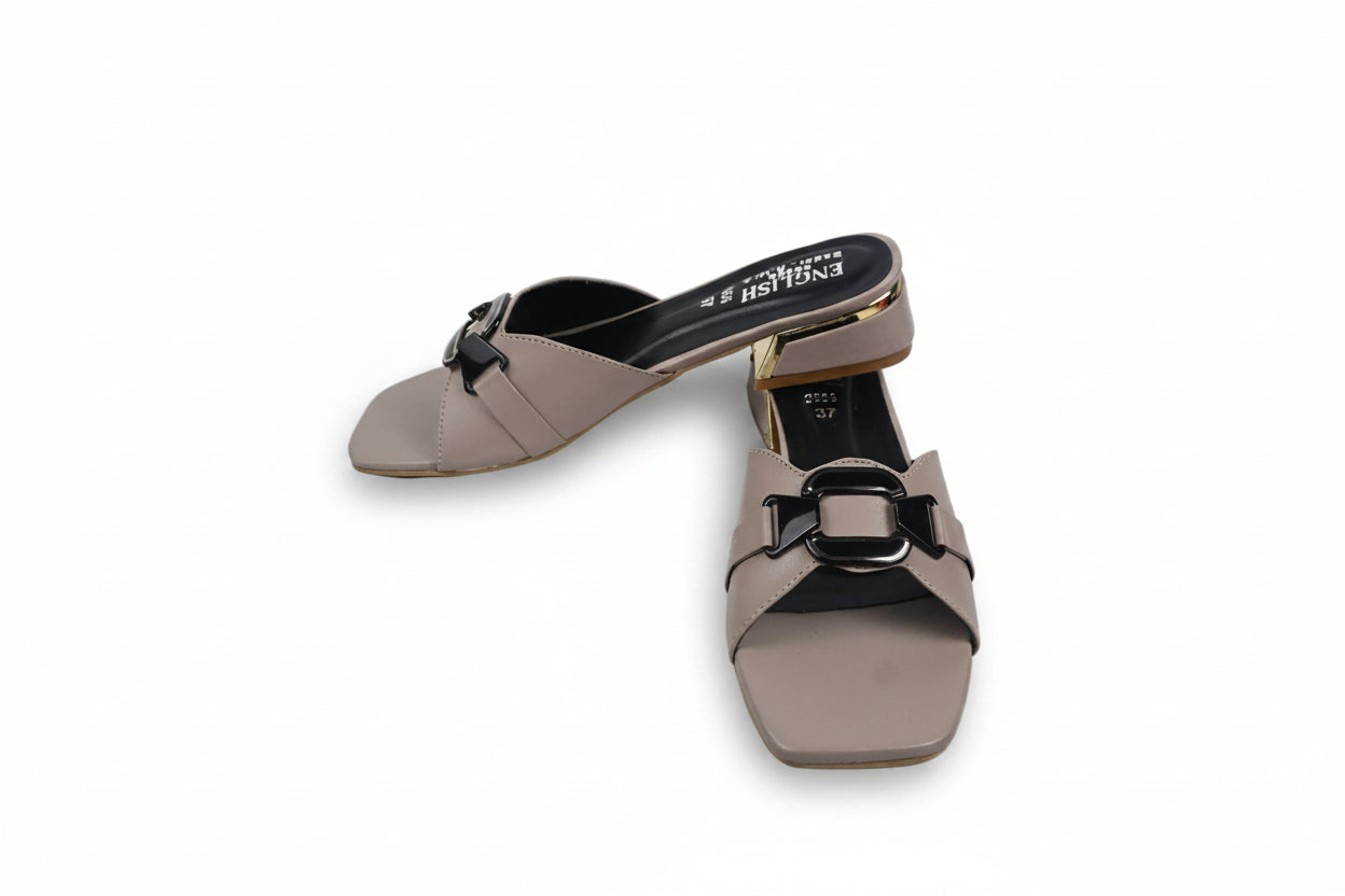 A pair of women's square-toe mule sandals in taupe with black buckle details and a gold-toned heel accent, shown on a white studio floor.