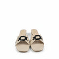 A pair of beige slide sandals with a prominent black metal buckle detail across the strap, displayed on a light gray surface.