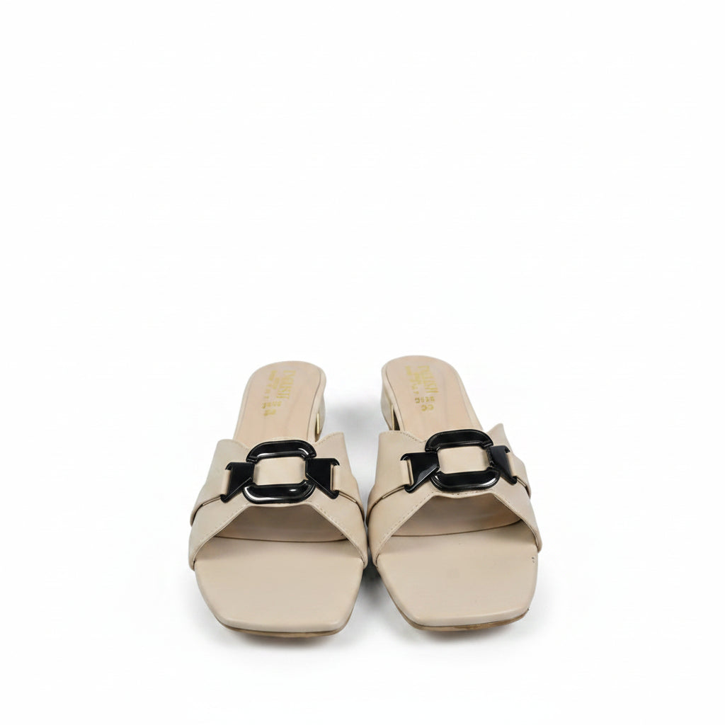 A pair of beige slide sandals with a prominent black metal buckle detail across the strap, displayed on a light gray surface.