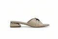 A single beige leather mule sandal with a low block heel, featuring a decorative black bow on the strap and a metallic gold accent on the heel, shown against a light gray background.