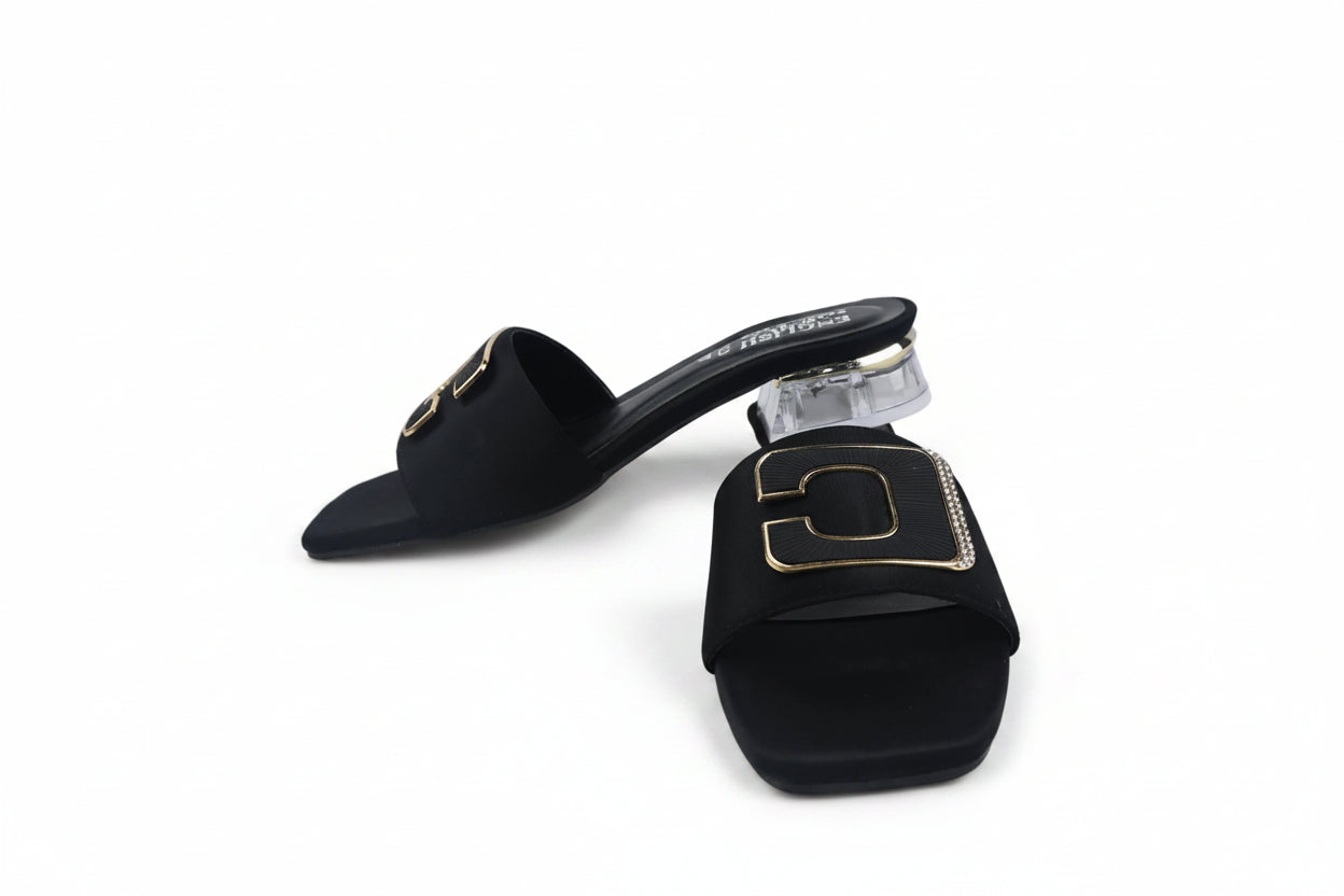 A pair of black slide sandals with chunky block heels and gold-tone metal hardware, displayed on a light gray surface.