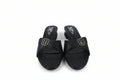 A pair of black slide sandals with textured straps and gold-tone square buckles, shown on a light gray background.
