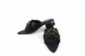A pair of black leather pointed-toe mule sandals with chunky gold-tone chain embellishments across the straps, displayed on a light gray floor.